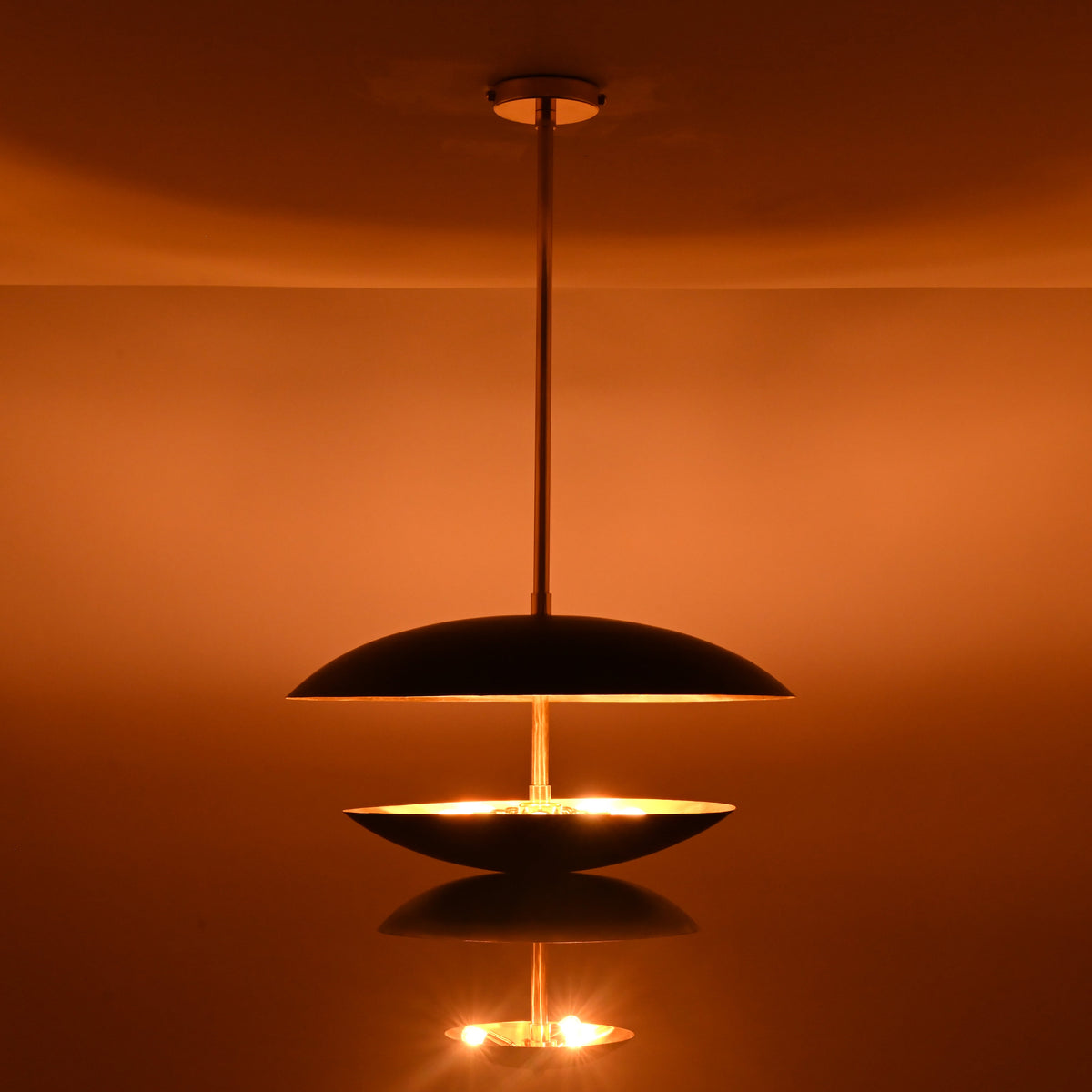 Black and brass disc chandelier showing illuminated lower bowl with soft diffused light