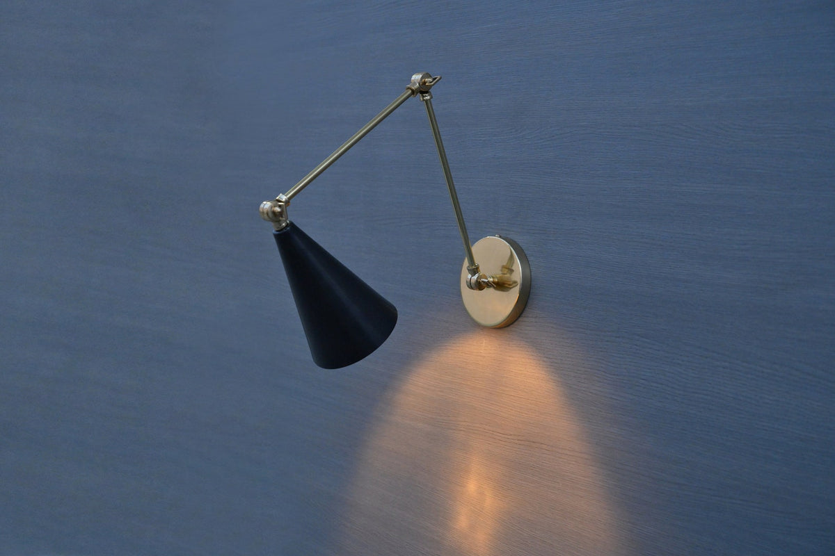 Modern brass wall sconce with black cone shade and swing arm casting warm light