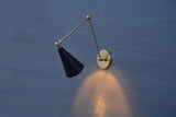 Modern brass wall sconce with black cone shade and swing arm casting warm light