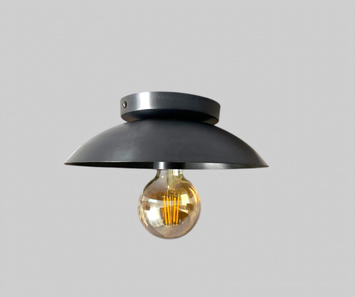 Close view of handcrafted blackened brass flush mount ceiling light featuring dome shade and Edison bulb by Brass Leaf Studio.