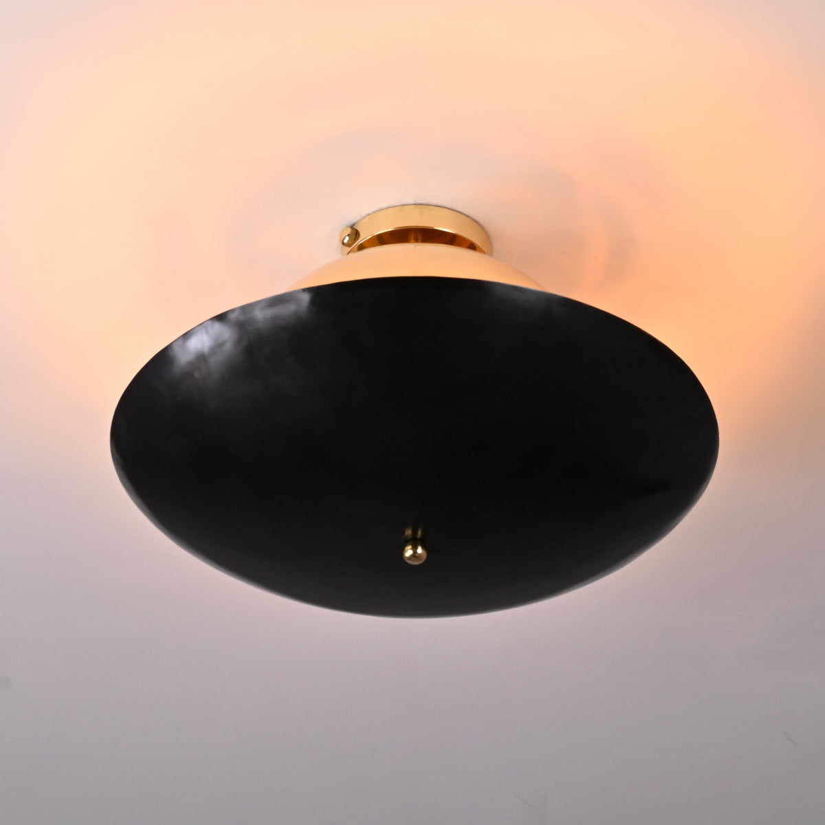 Bottom view of mixed-finish brass flushmount with blackened lower bowl and soft warm illumination from the polished brass upper dome.