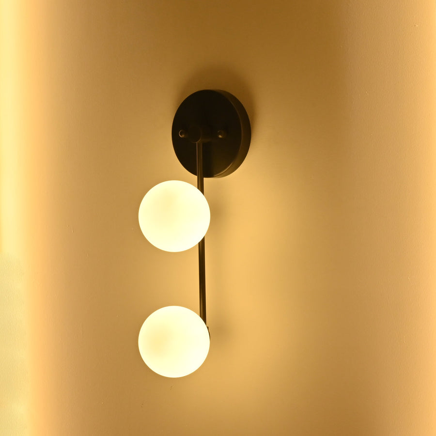 Two-light globe wall sconce illuminated with soft warm ambient light for bedroom, hallway, vanity, or living room interiors