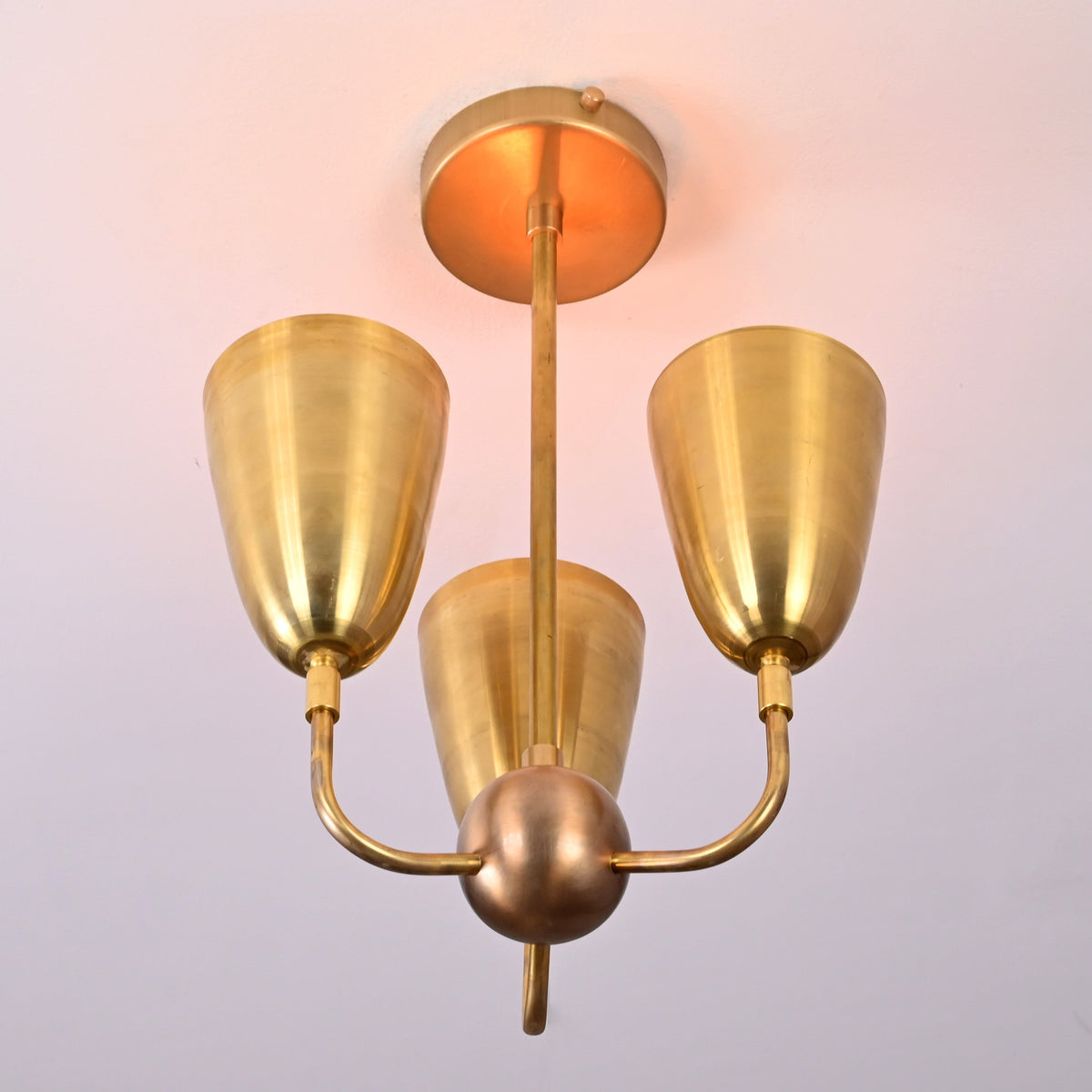 Bottom angle view of brass three-light ceiling fixture featuring sculpted cup shades and mid-century styling.