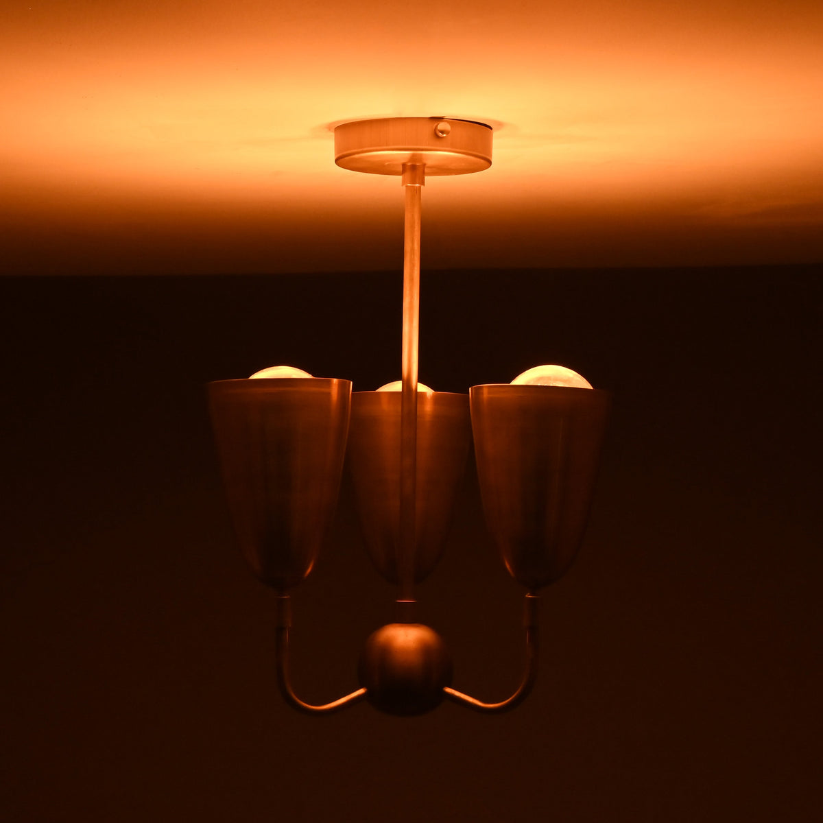 Brass 3-light chandelier emitting soft warm illumination, showcasing elegant cup shades and a minimalist brass stem.