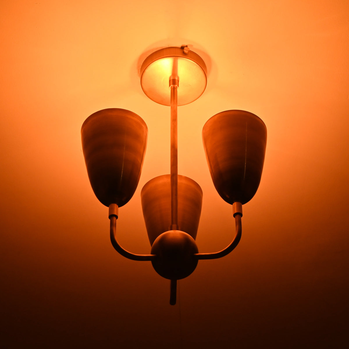 Warm backlit view of three-light brass flushmount chandelier highlighting indirect glow and vintage aesthetic.