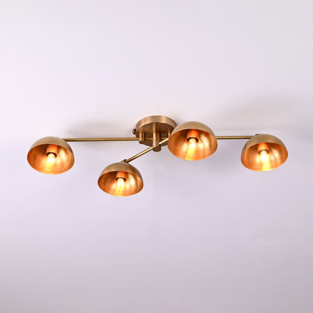 Contemporary 4-light brass flushmount chandelier featuring adjustable arms and warm glowing dome shades, minimalist ceiling light.