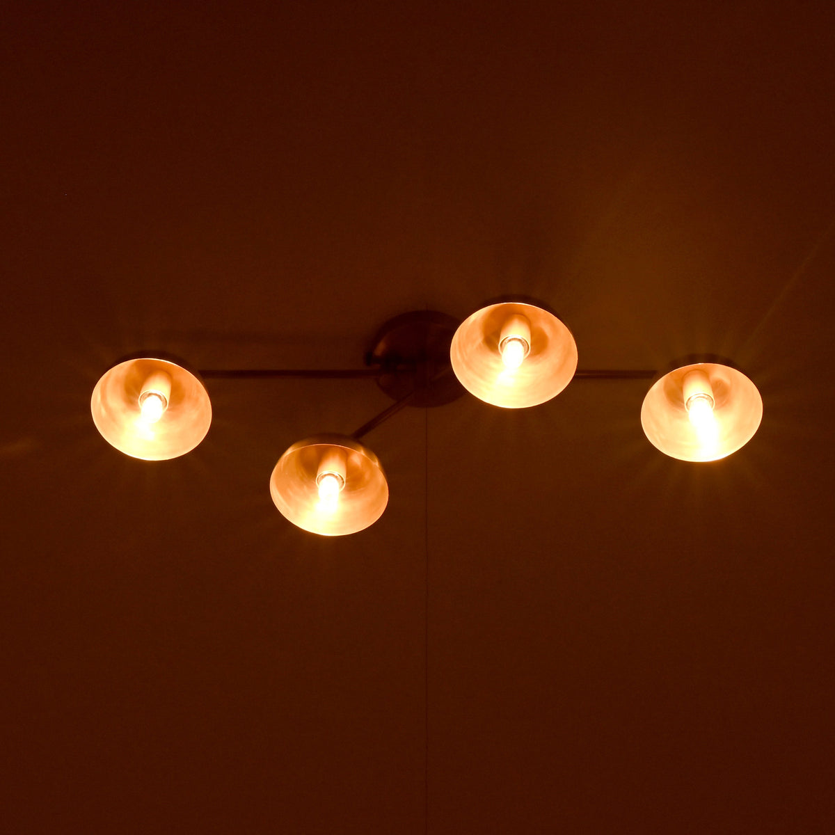 Brass 4-light ceiling fixture glowing warmly in a dark room, bowl shades casting soft ambient illumination.