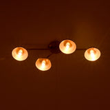 Brass 4-light ceiling fixture glowing warmly in a dark room, bowl shades casting soft ambient illumination.