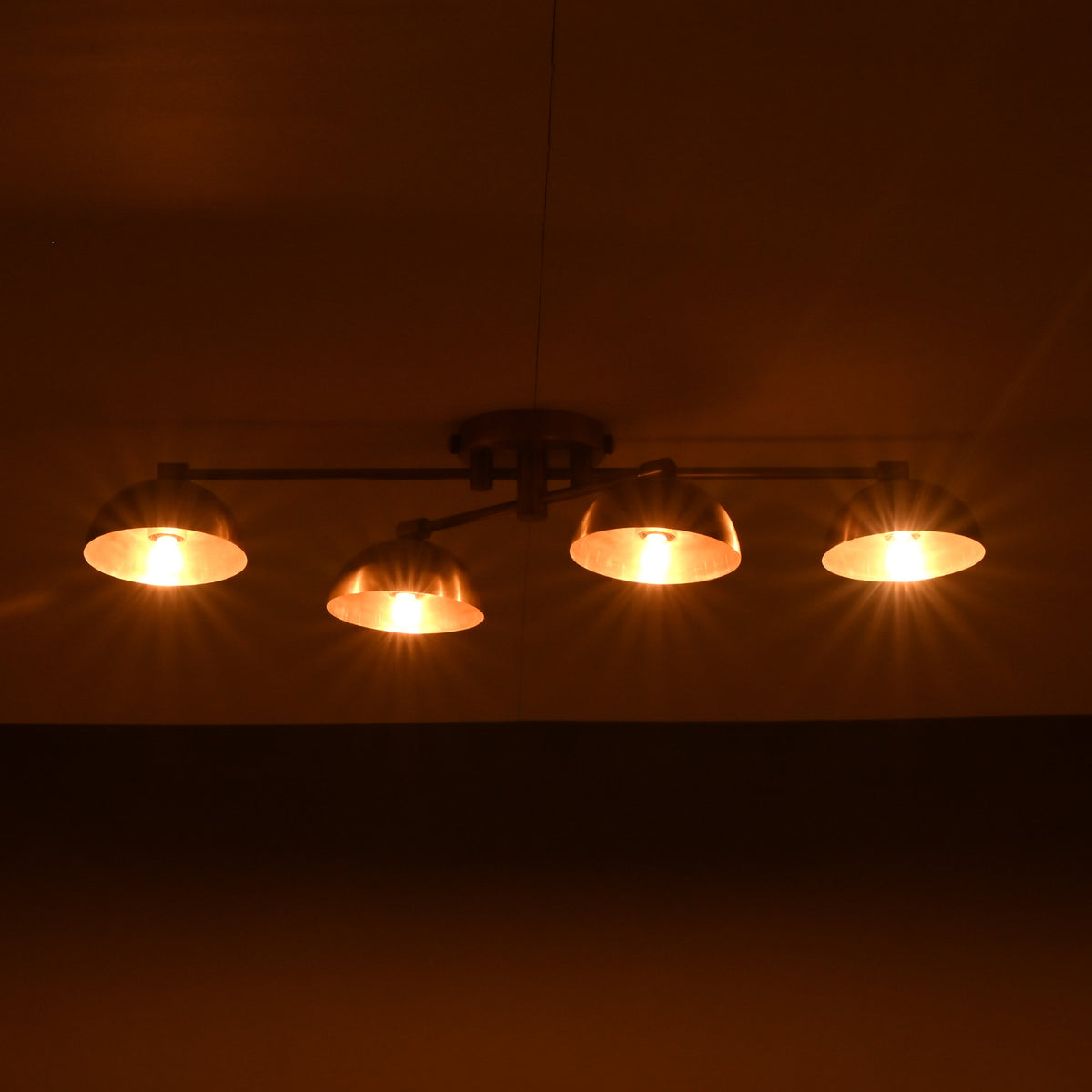 Low-profile handmade brass chandelier with four illuminated dome shades, casting golden lighting on the ceiling.