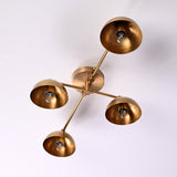 : Brass flushmount chandelier with four glowing bowl shades in a warm-lit environment, modern handcrafted ceiling fixture.