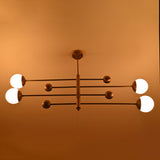 Front view of warm-lit brushed brass chandelier with linear arms and opal glass globes.