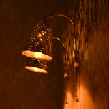 Angled view of brass bell wall sconces glowing, creating patterned reflections on the wall