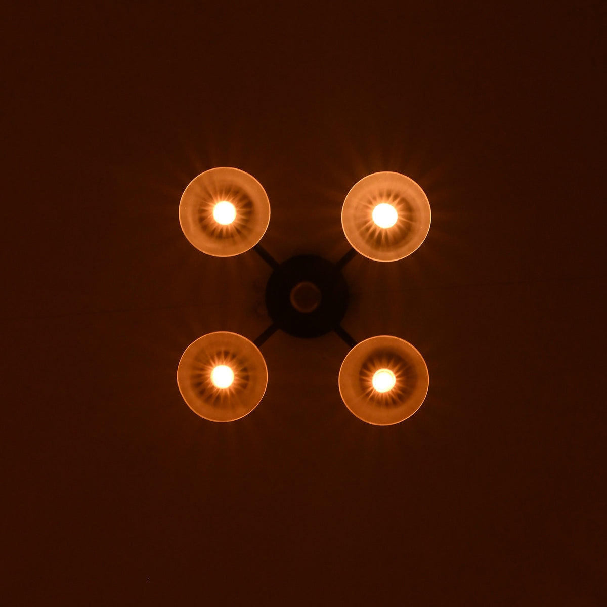 Four light brass bowl ceiling fixture casting warm ambient glow in a dark interior setting.