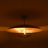 Warm brass ceiling light with bowl-shaped lower disc illuminated in a dark room