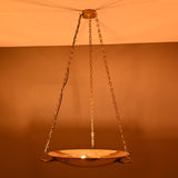Brass bowl pendant light hanging from chains, glowing warmly in a dim interior