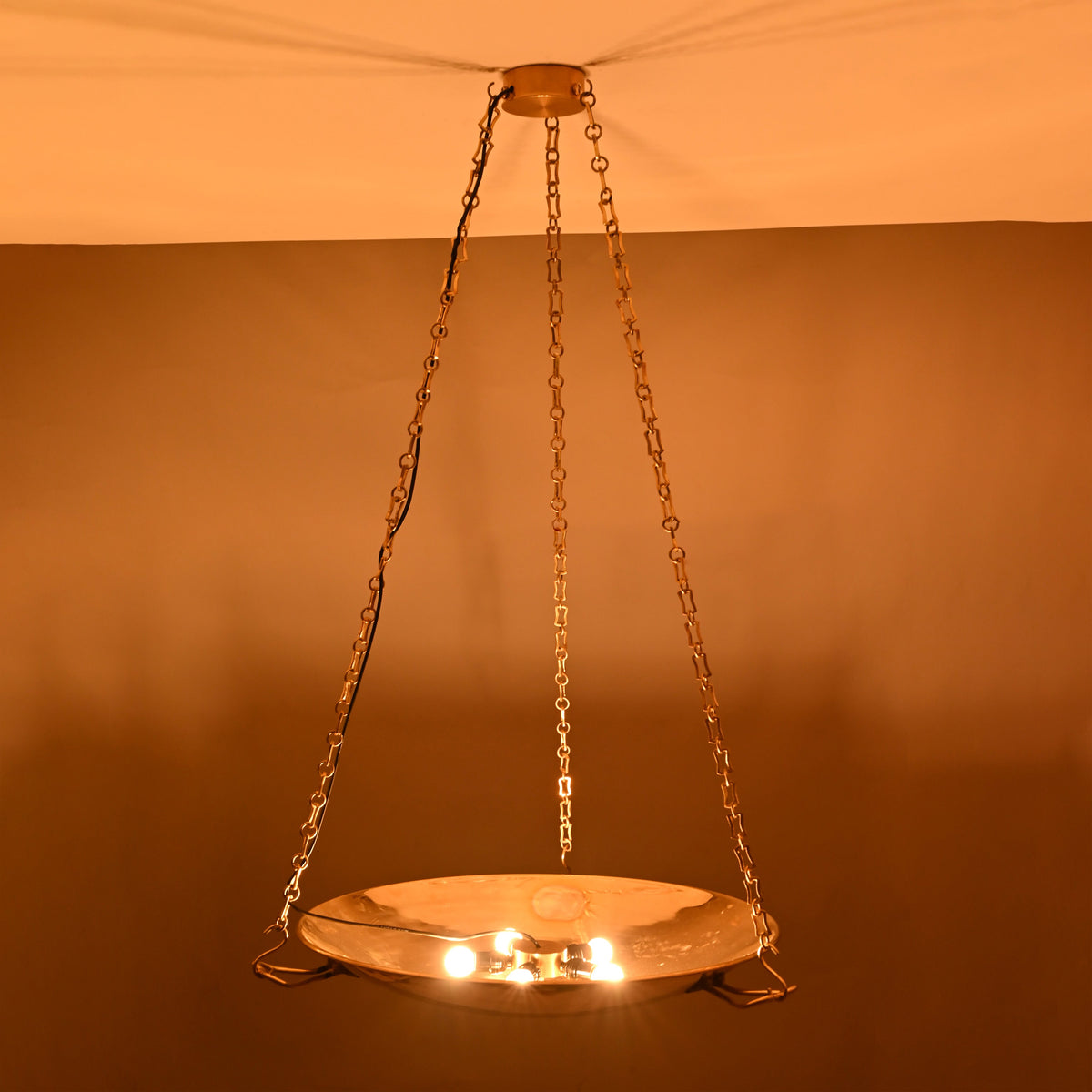 Night view of brass bowl chandelier showing soft uplighting and chain-supported design