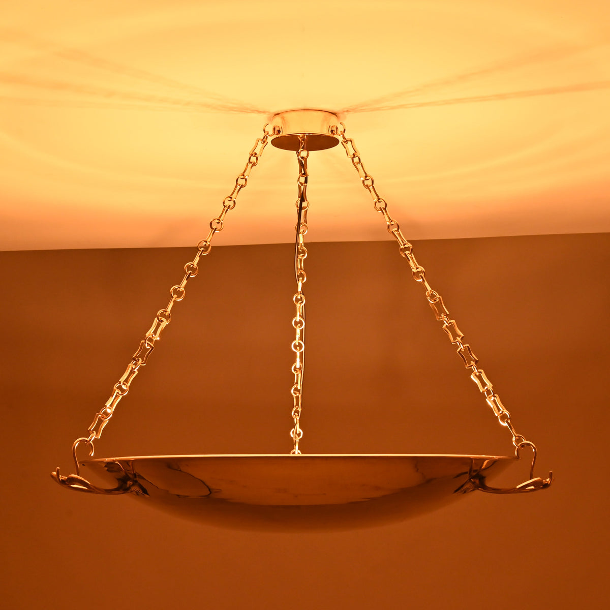 Brass bowl chandelier glowing warmly with indirect ceiling illumination and decorative brass chains