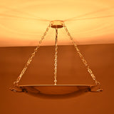 Brass bowl chandelier glowing warmly with indirect ceiling illumination and decorative brass chains