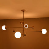 Side angle of illuminated brass chandelier showing warm glowing opal globes and modern linear form.