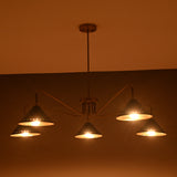 Evening ambience view of brass cone chandelier with five perforated black shades casting warm diffused light.