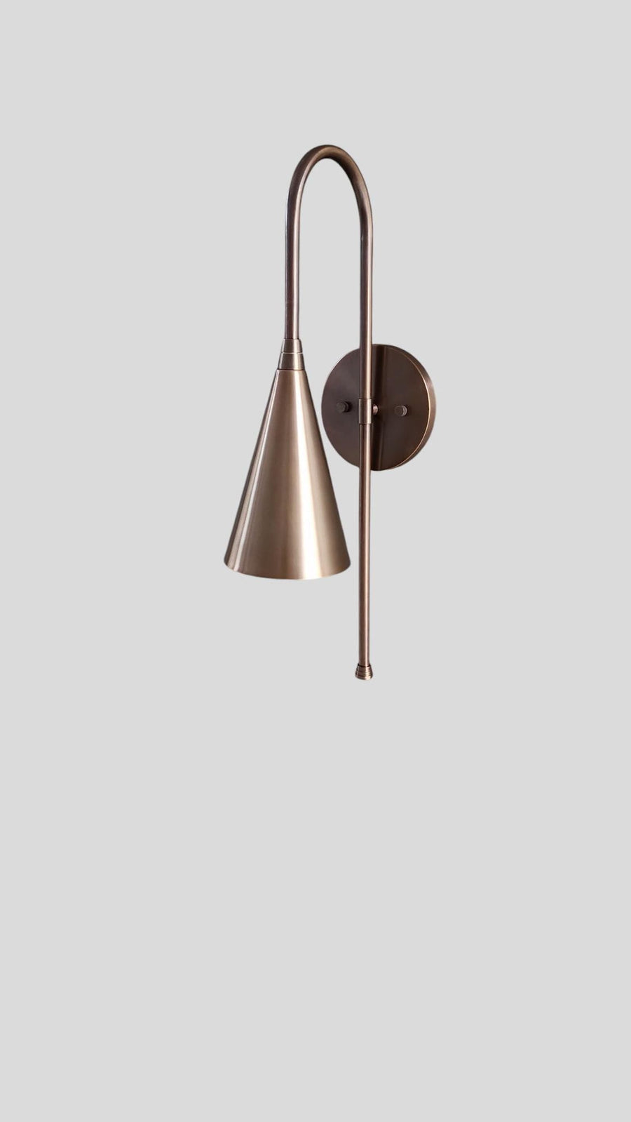 Front view of handmade brass wall sconce with cone shade emitting warm light