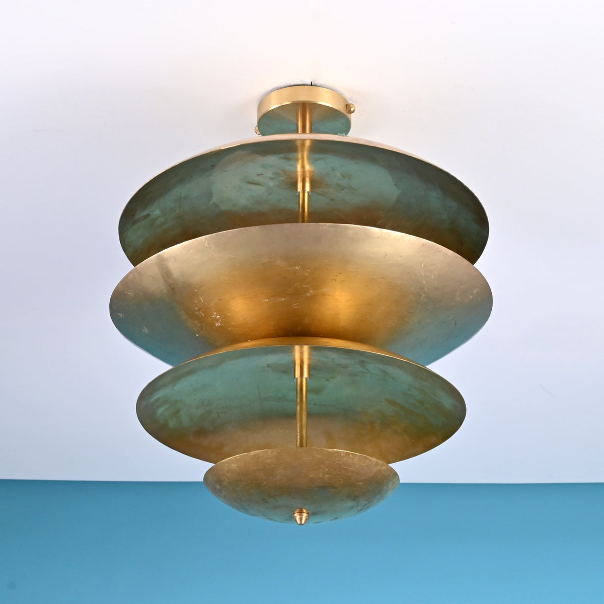Low angle view of handcrafted brass disc ceiling light highlighting layered bowl shades and warm indirect illumination.