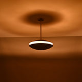 Wide-view shot of brass disc chandelier in a dark room, casting a soft halo of warm indirect light across the ceiling.