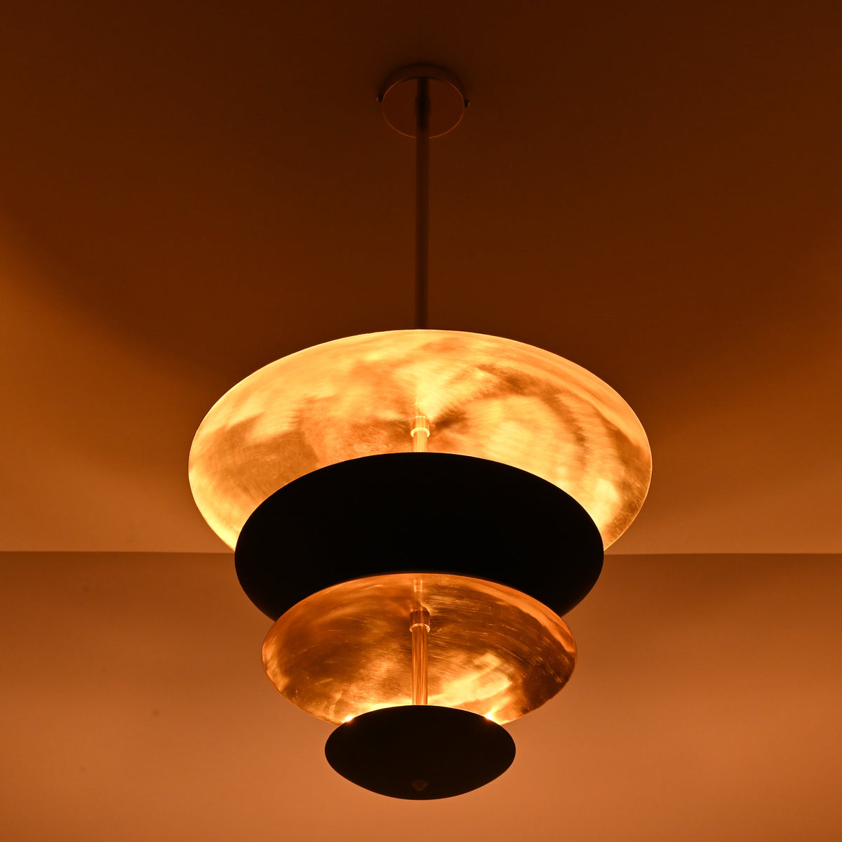 Close-up of layered brass disc chandelier with dramatic warm lighting and handcrafted metal finish