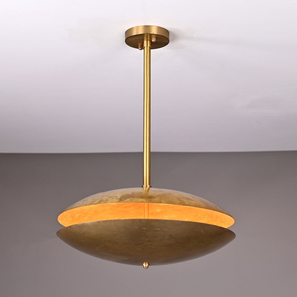 Brass disc chandelier illuminated from within, showing warm golden glow highlighting the textured hammered brass finish and sculptural form.