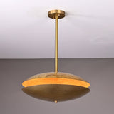 Brass disc chandelier illuminated from within, showing warm golden glow highlighting the textured hammered brass finish and sculptural form.