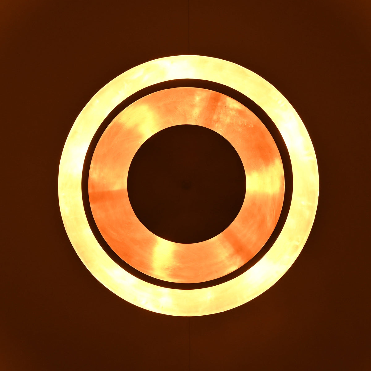 Bottom glowing ring view of layered brass disc chandelier illuminated with warm ambient lighting.