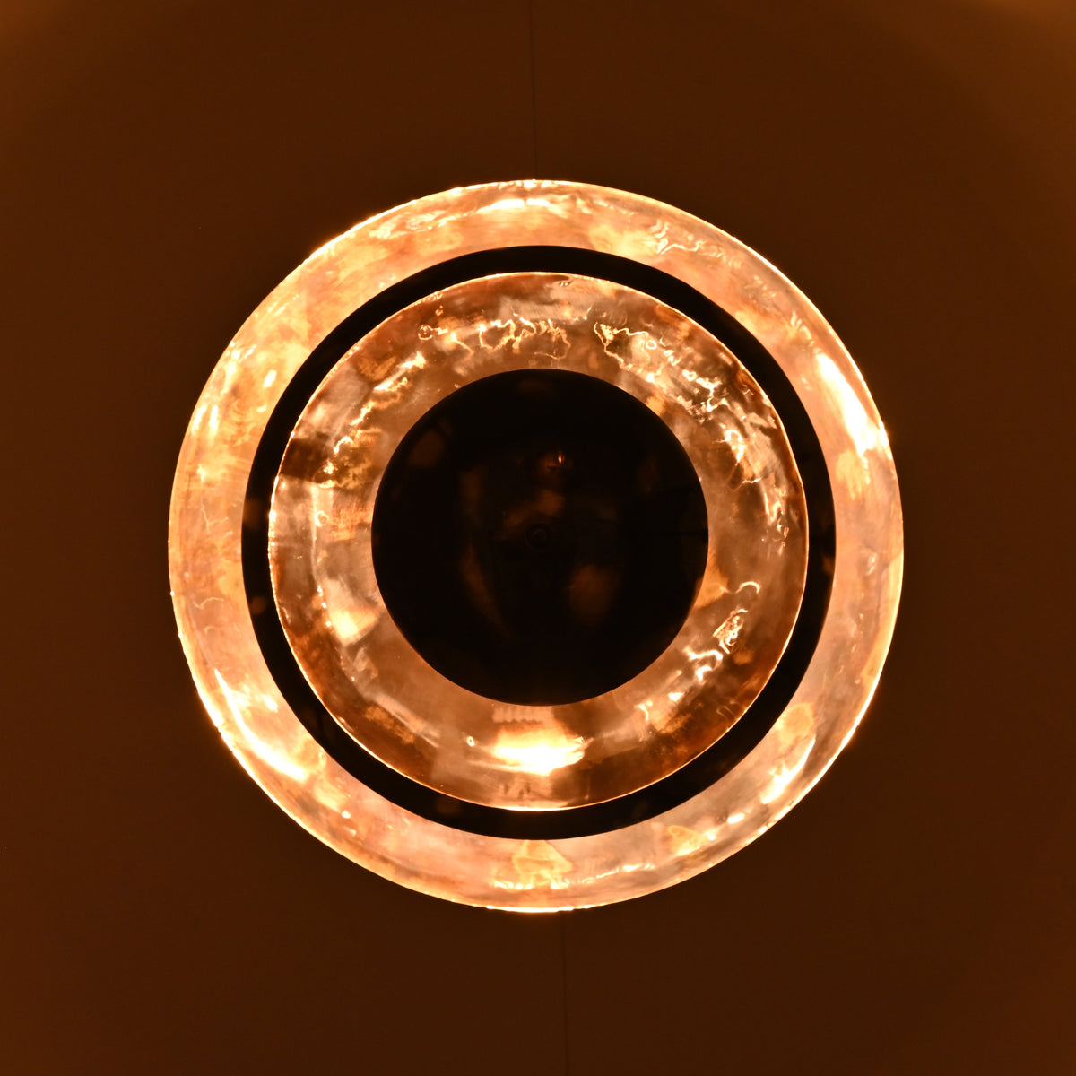 Glowing night view of multi-tier brass disc chandelier with warm indirect lighting