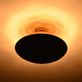 Mixed-finish brass flushmount in a dark room, showing strong warm halo lighting effect above the fixture.