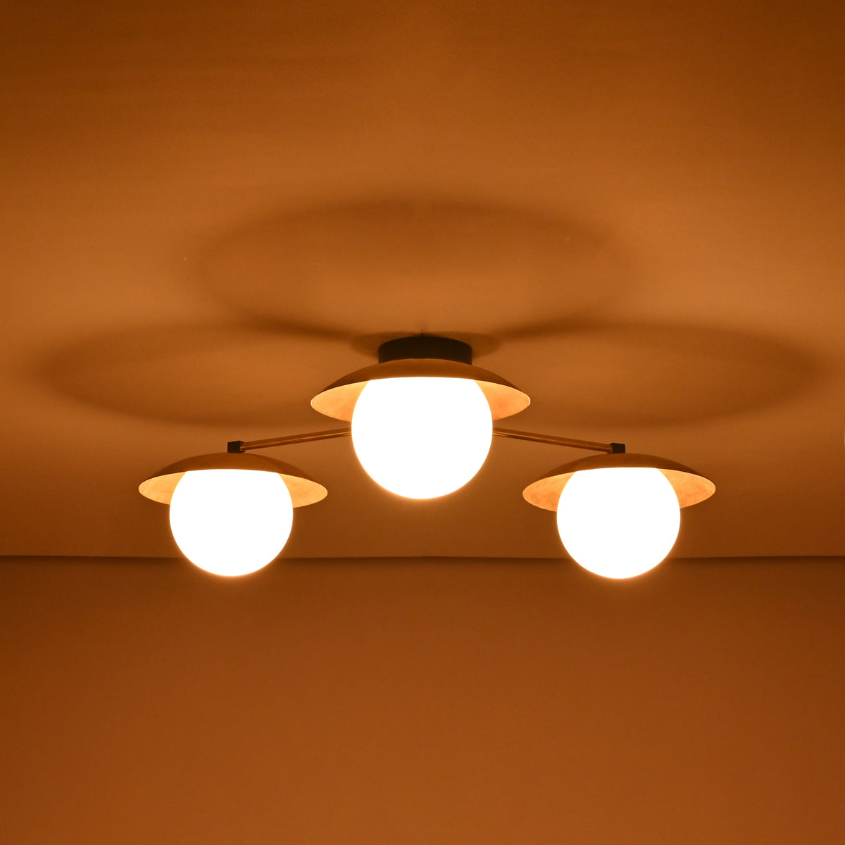 3 light brass disc flush mount ceiling light emitting a soft warm glow in a low light setting.