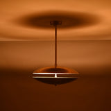 Brass disc pendant light with narrow slit illumination glowing in a warm amber tone, showcasing dramatic ambient lighting in the dark.