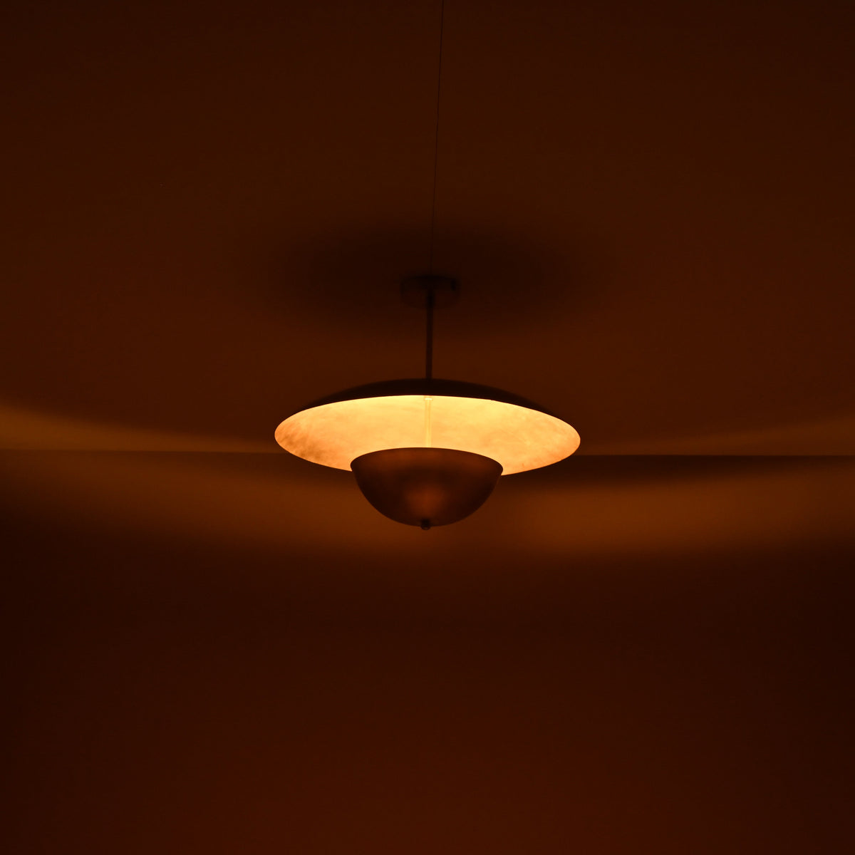 Warm ambient lighting from brass disc chandelier showing indirect uplight effect in a dim interior
