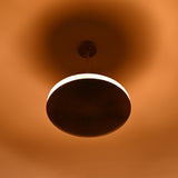 Brass disc pendant light photographed in low light, showing bright illuminated ring and soft ambient glow on ceiling and surroundings.