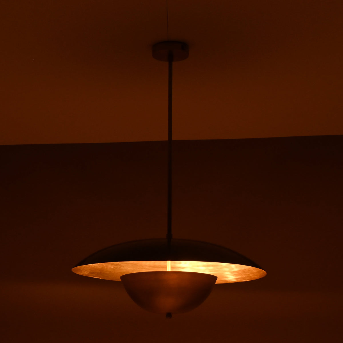 Side angle of handmade brass pendant glowing in warm ambient light with minimalistic industrial appeal