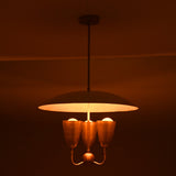 Warm ambient brass pendant chandelier with wide dome shade and three brass light cups creating soft atmospheric lighting.