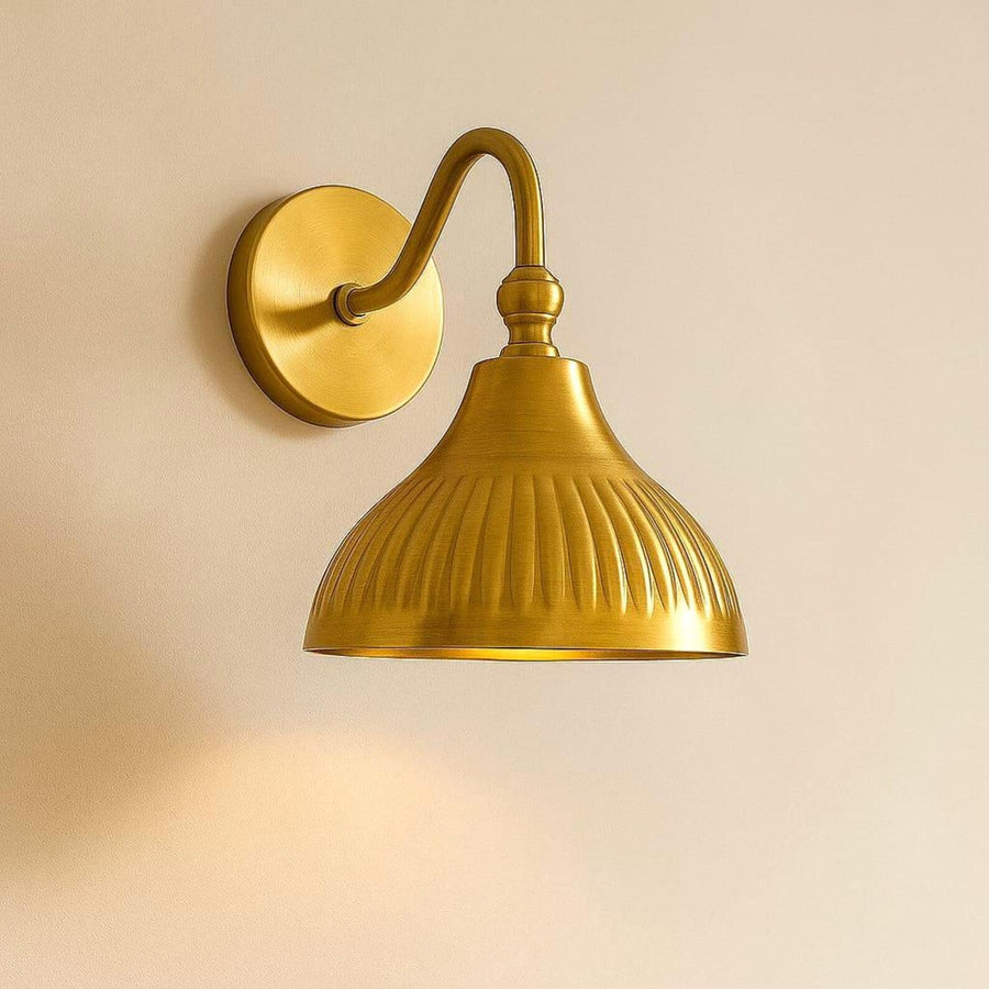 Modern brushed brass fluted dome wall sconce with curved arm mounted on warm peach textured wall background.