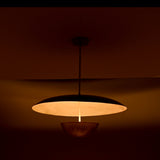 Warm-lit side view of dual-shade brass pendant casting soft ambient light through its sculptural dome and bowl.