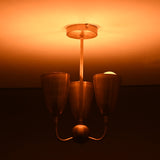 Brass flushmount chandelier with warm ambient lighting and sculpted triple cup design, mid-century modern fixture.