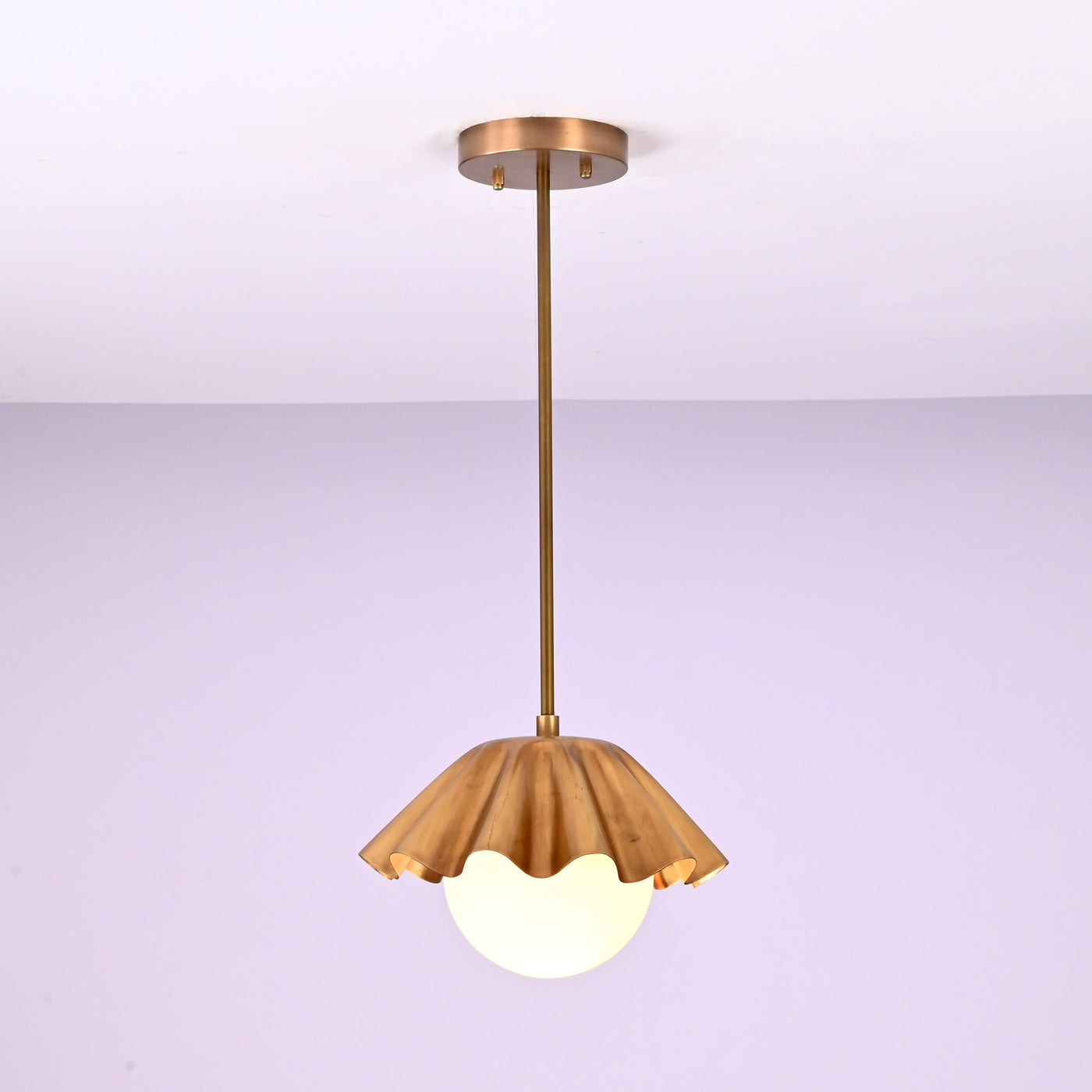 Minimalist brass fluted pendant light hanging straight with sculpted shade and glowing globe.