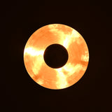 Brass disc lighting fixture illuminated at night showing warm indirect ambient glow