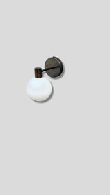 Angled view of industrial style brass wall sconce with opal glass light