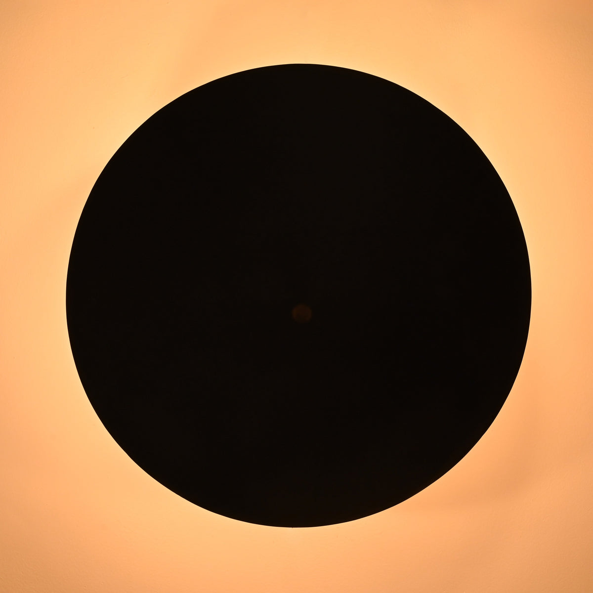 Bottom view of a matte black bowl ceiling light casting a circular warm halo of light on the ceiling.