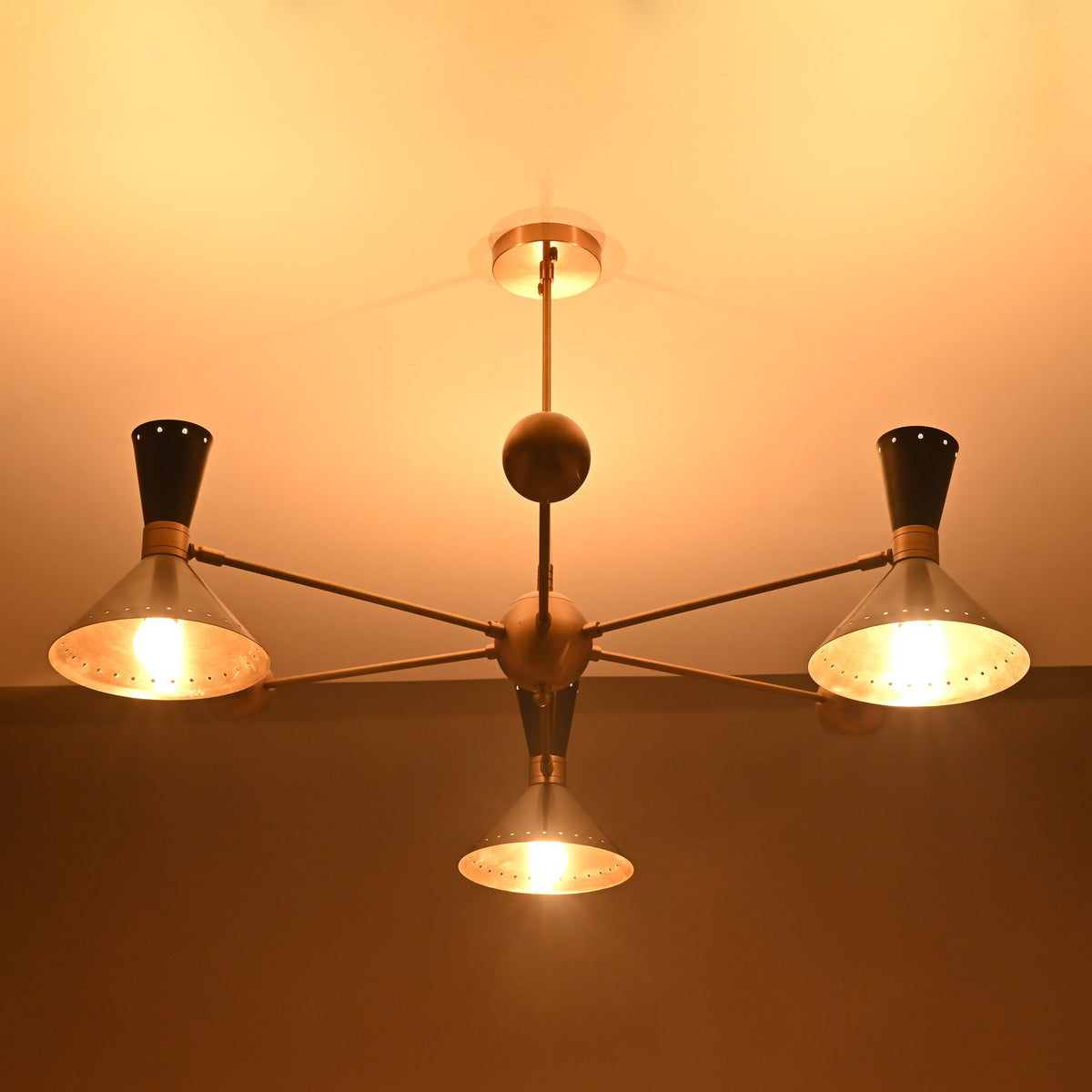 Illuminated industrial brass cone shade chandelier showing warm glowing perforated shades by Brass Leaf Studio.