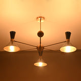 Illuminated industrial brass cone shade chandelier showing warm glowing perforated shades by Brass Leaf Studio.
