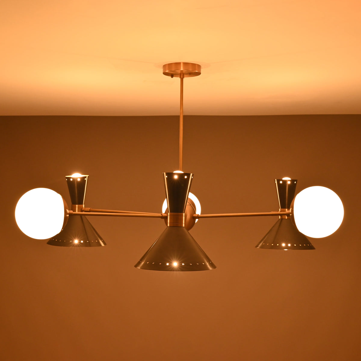 Night-time view of a mid-century brass chandelier with cone and globe lights casting a soft ambient glow.