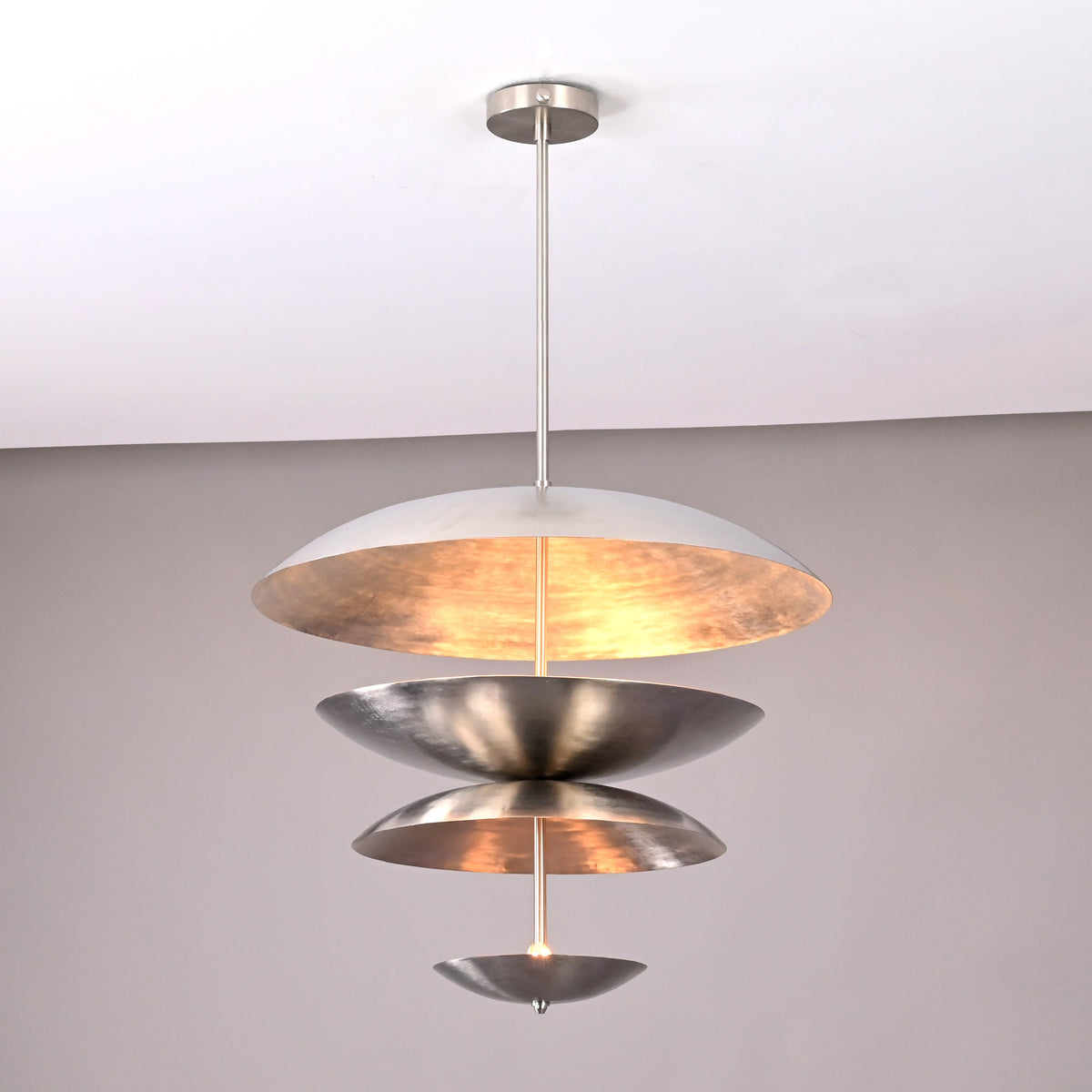 Silver-finish tiered metal disc pendant light featuring layered reflective bowls and warm interior glow.